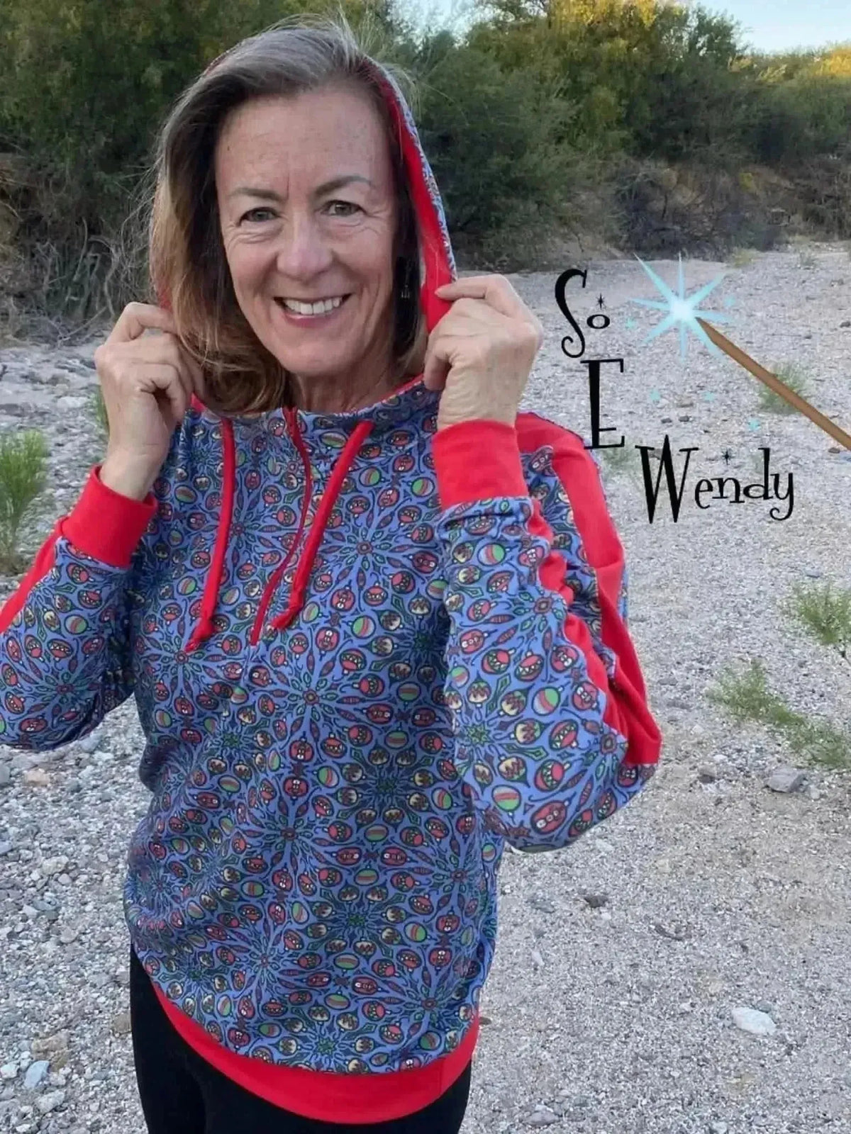 Woman modeling a navy hoodie with colorful floral print and red accents outdoors.