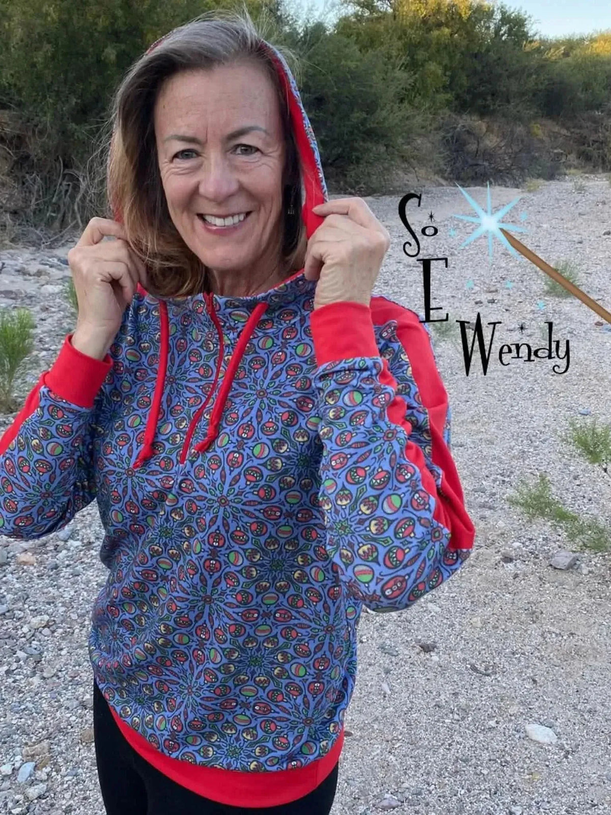 Woman modeling a navy hoodie with colorful floral print and red accents outdoors.