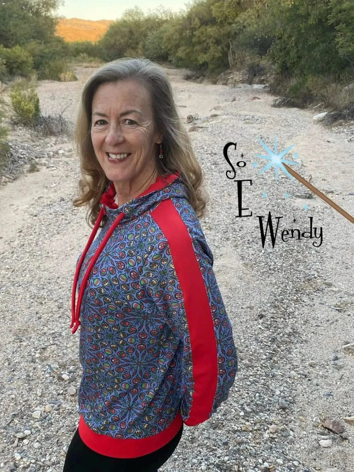 Woman modeling a red hooded sweatshirt with multicolored floral print and white side stripes.