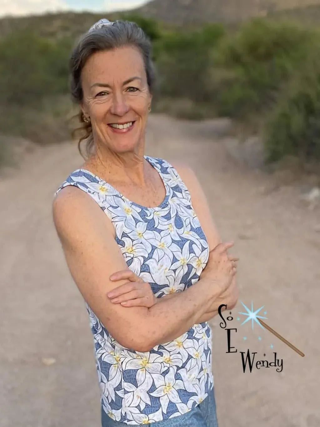 A woman wears a sleeveless top made from blue fabric with white lily flowers.