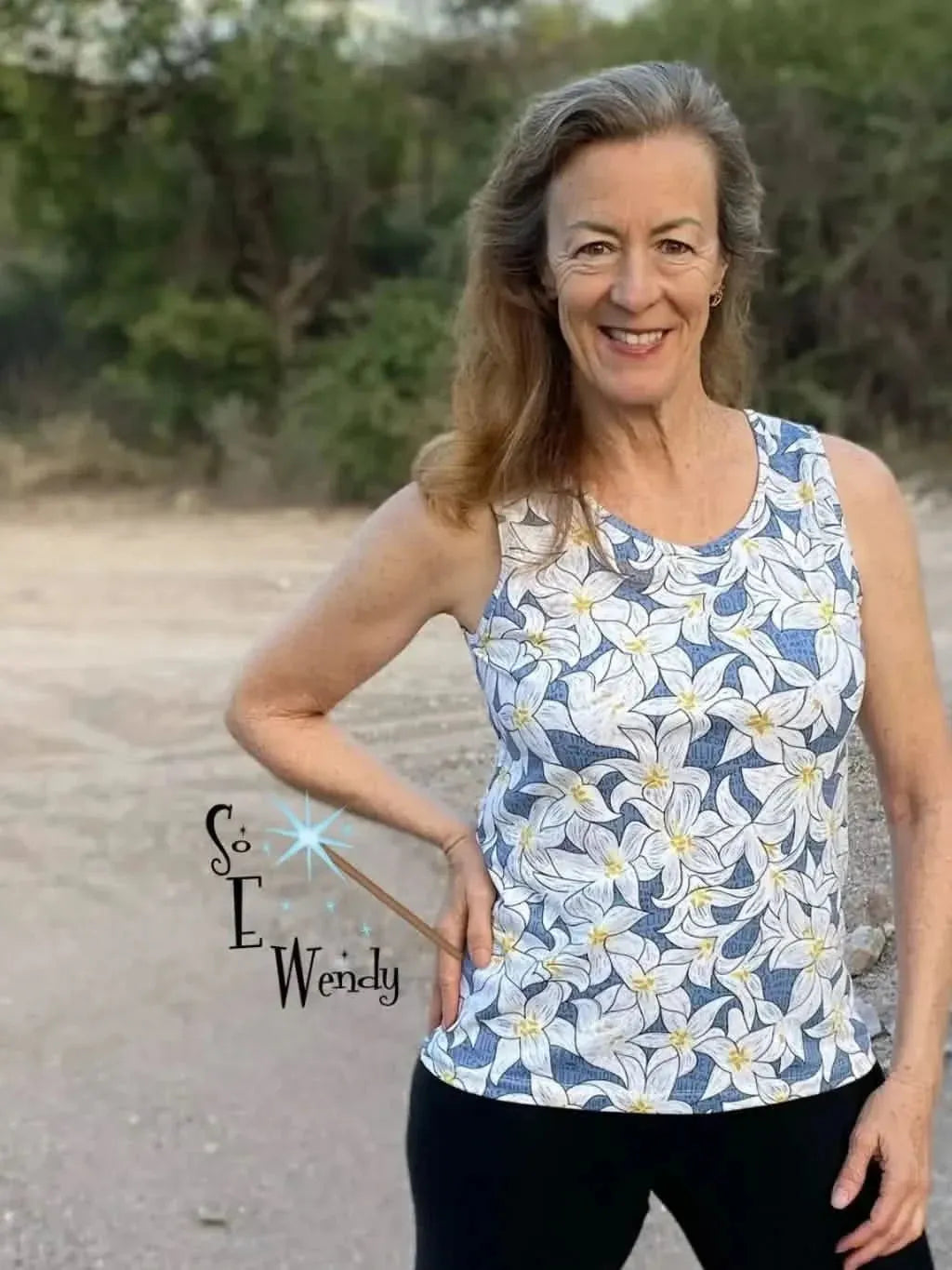 A woman smiles, wearing a tank top with a blue lilies floral print.