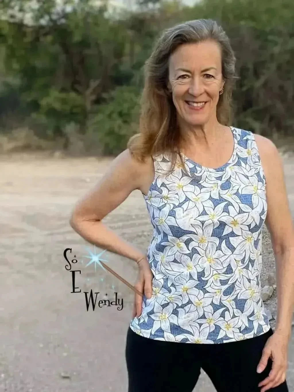 A woman smiles, wearing a tank top with a blue lilies floral print.