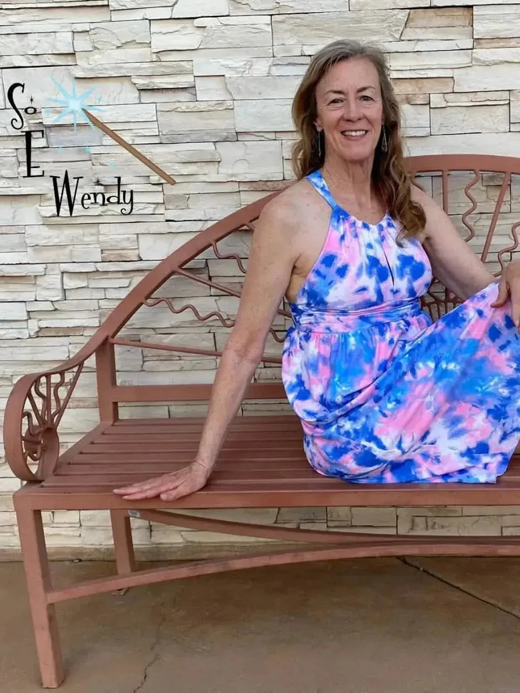 A woman sits on a bench wearing a dress made from bubblegum tie-dye fabric.