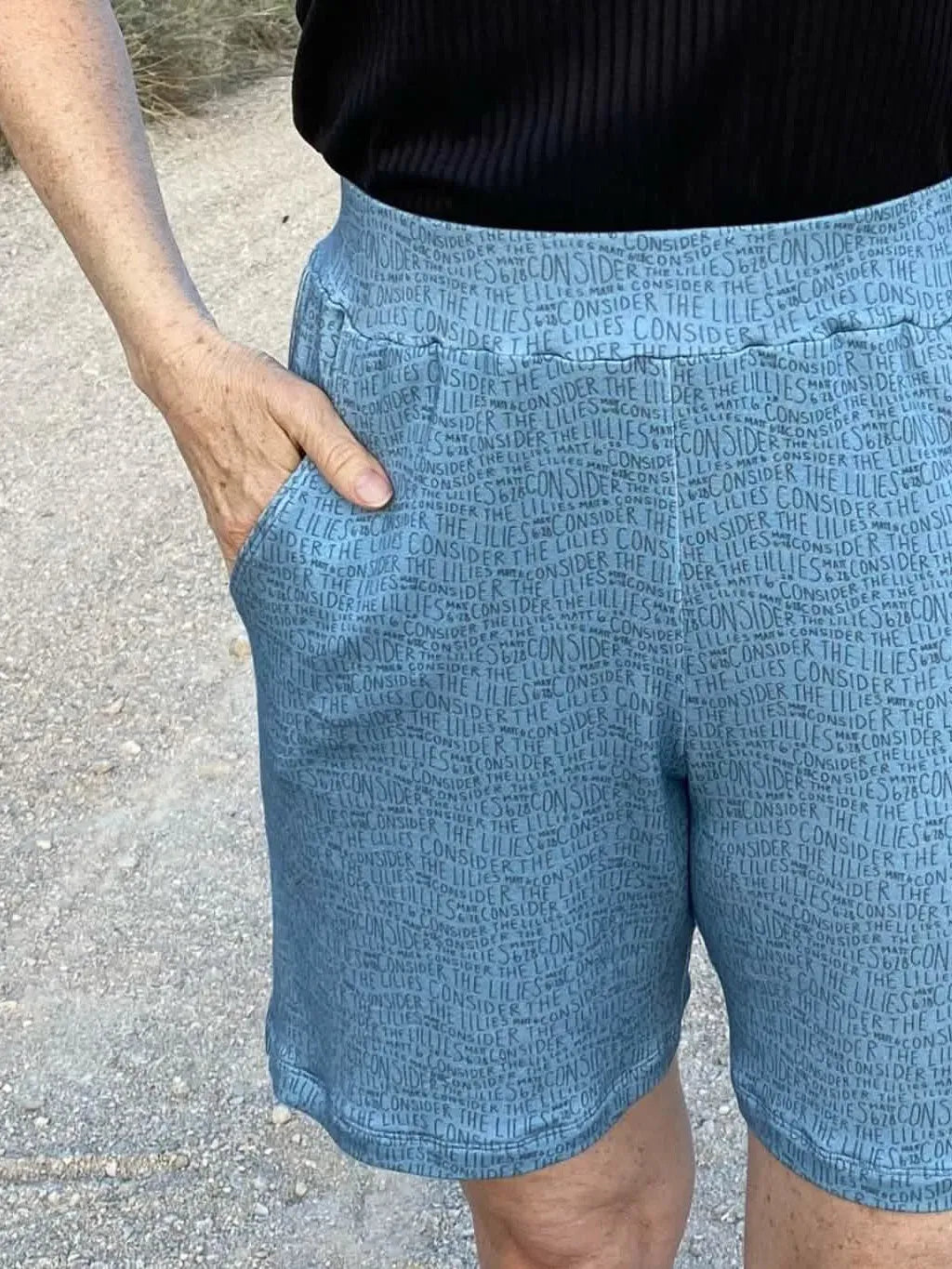 A person wears blue shorts with "Consider the Lilies" text printed on them.
