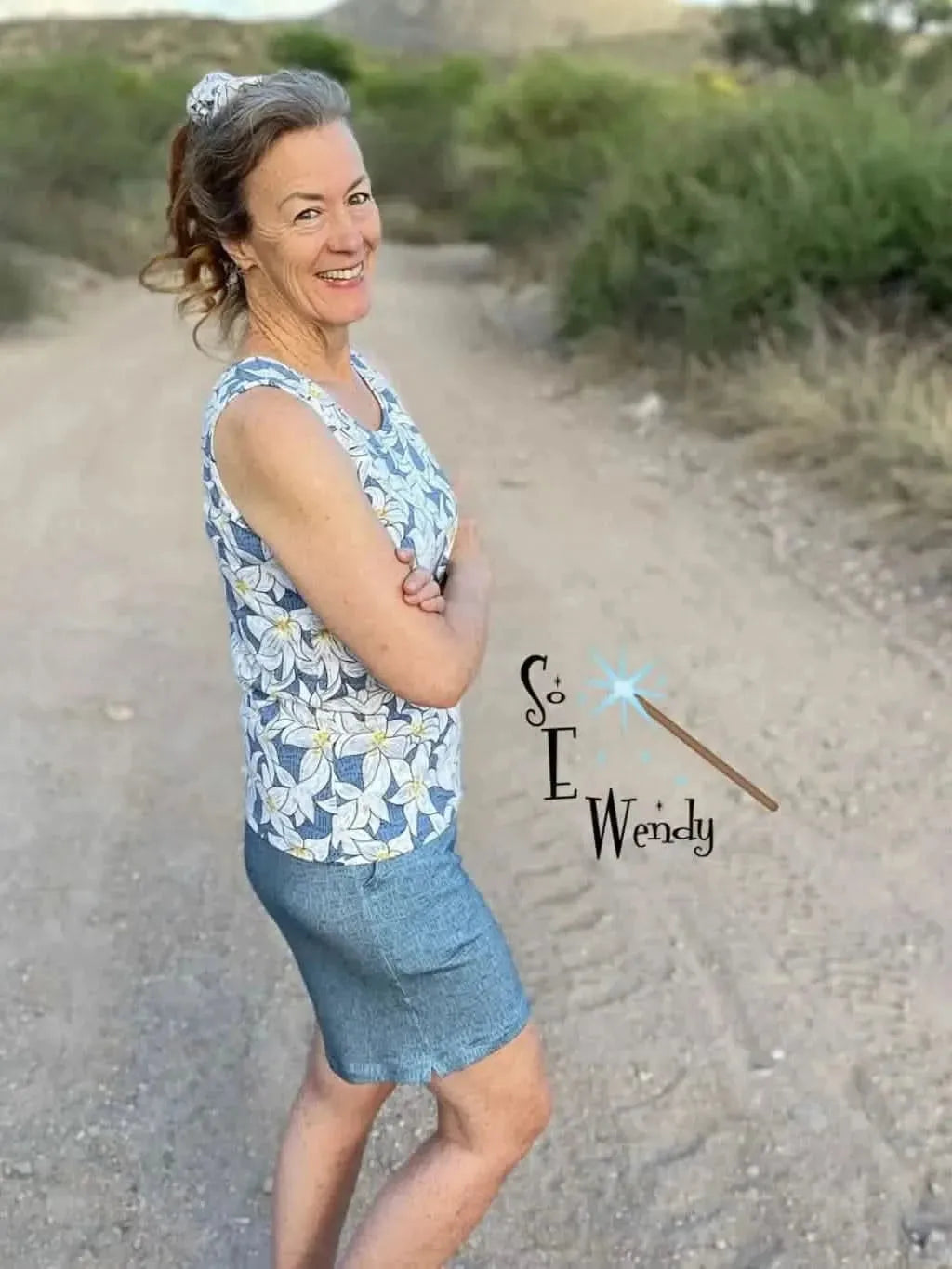 A woman wears a blue and white floral print sleeveless top and a denim skirt.