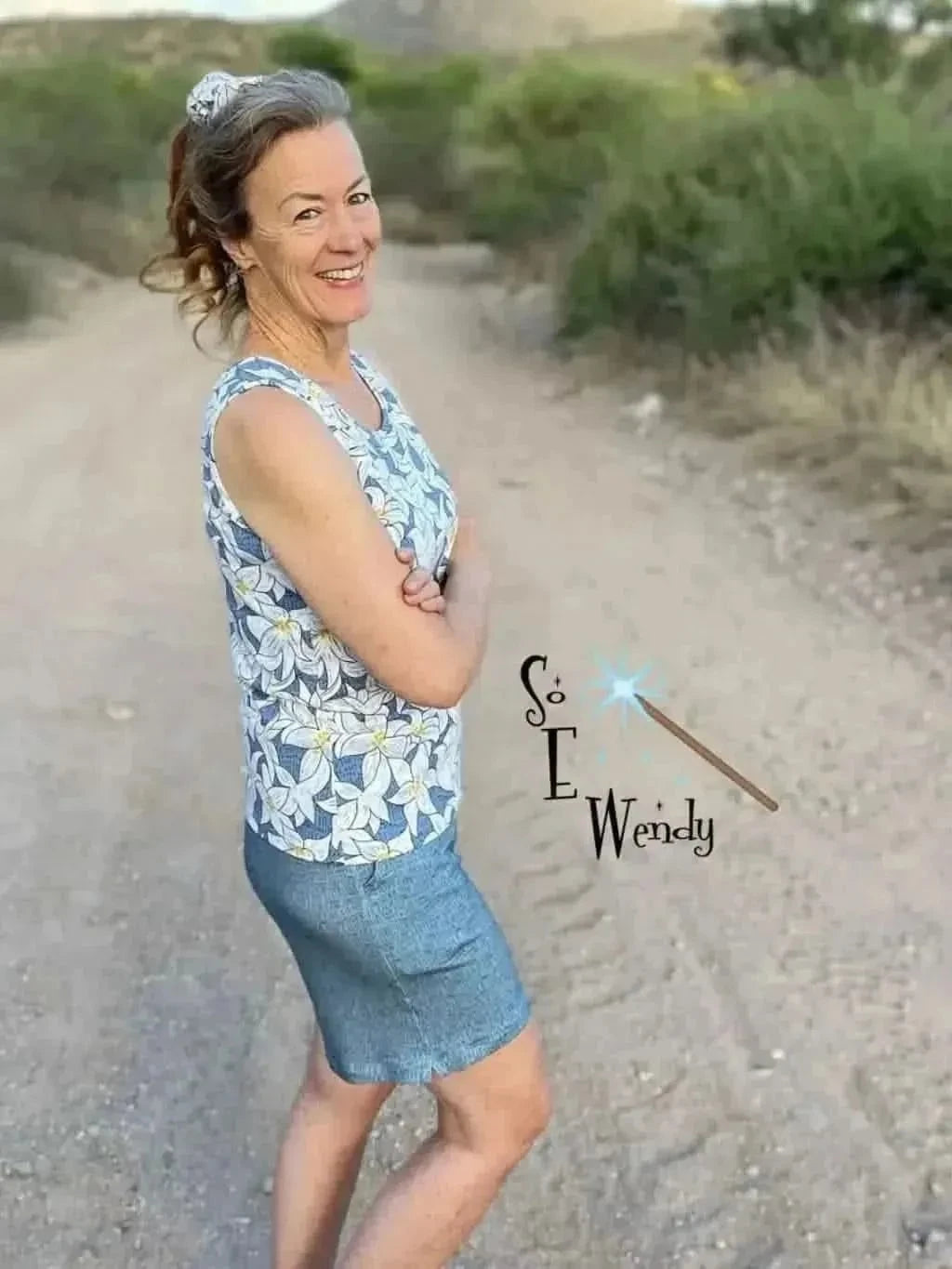A woman wears a blue and white floral print sleeveless top and a denim skirt.