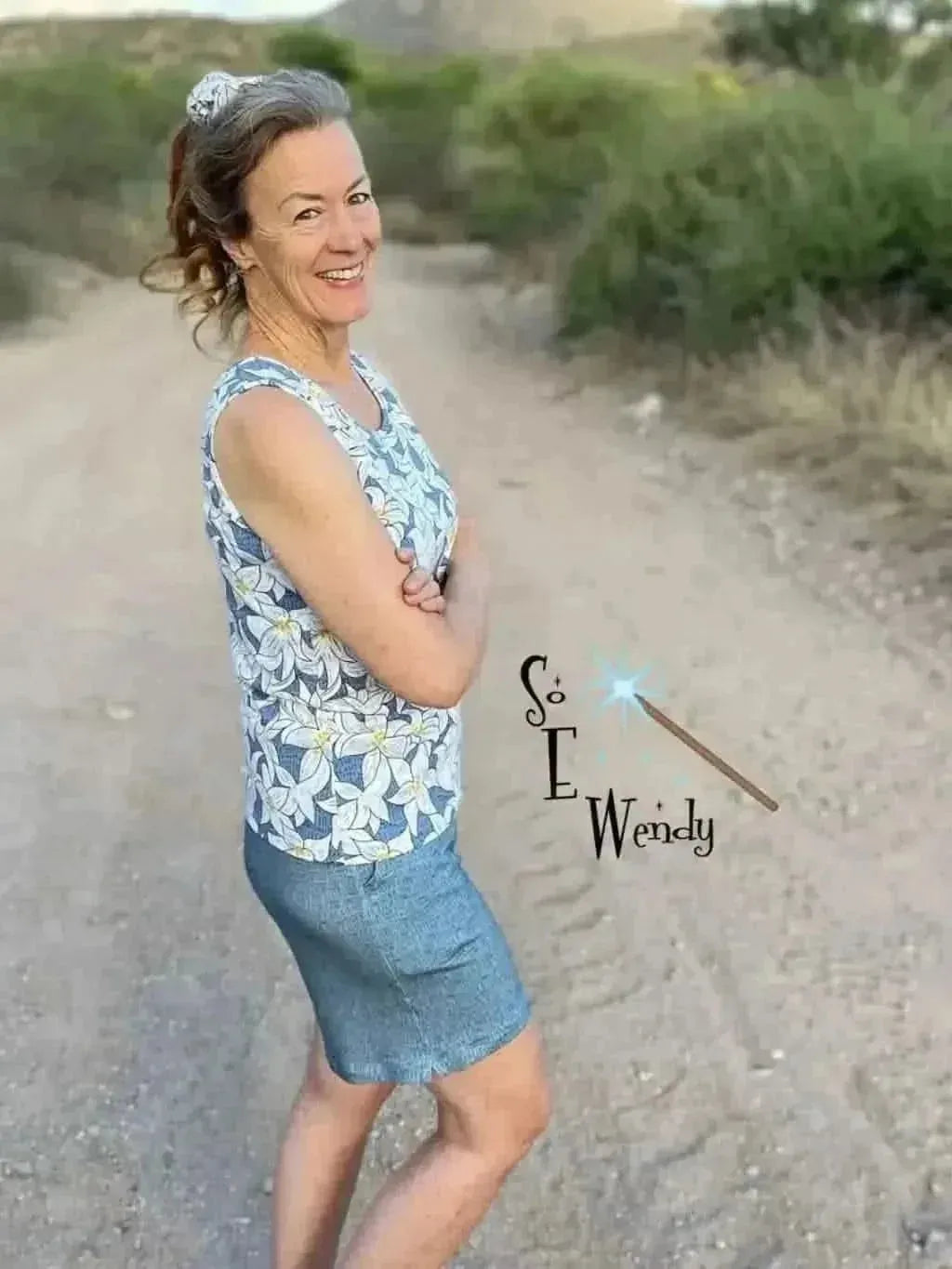 A woman wears a blue and white floral print sleeveless top and a denim skirt.