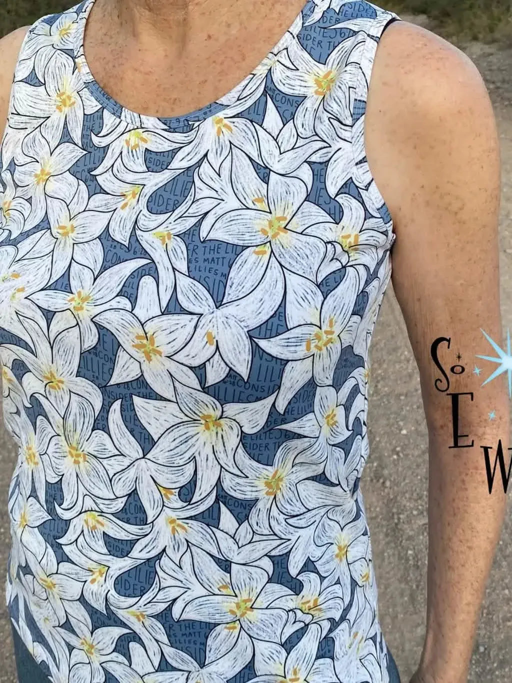 A person wears a tank top with a white lily floral pattern on a blue background.