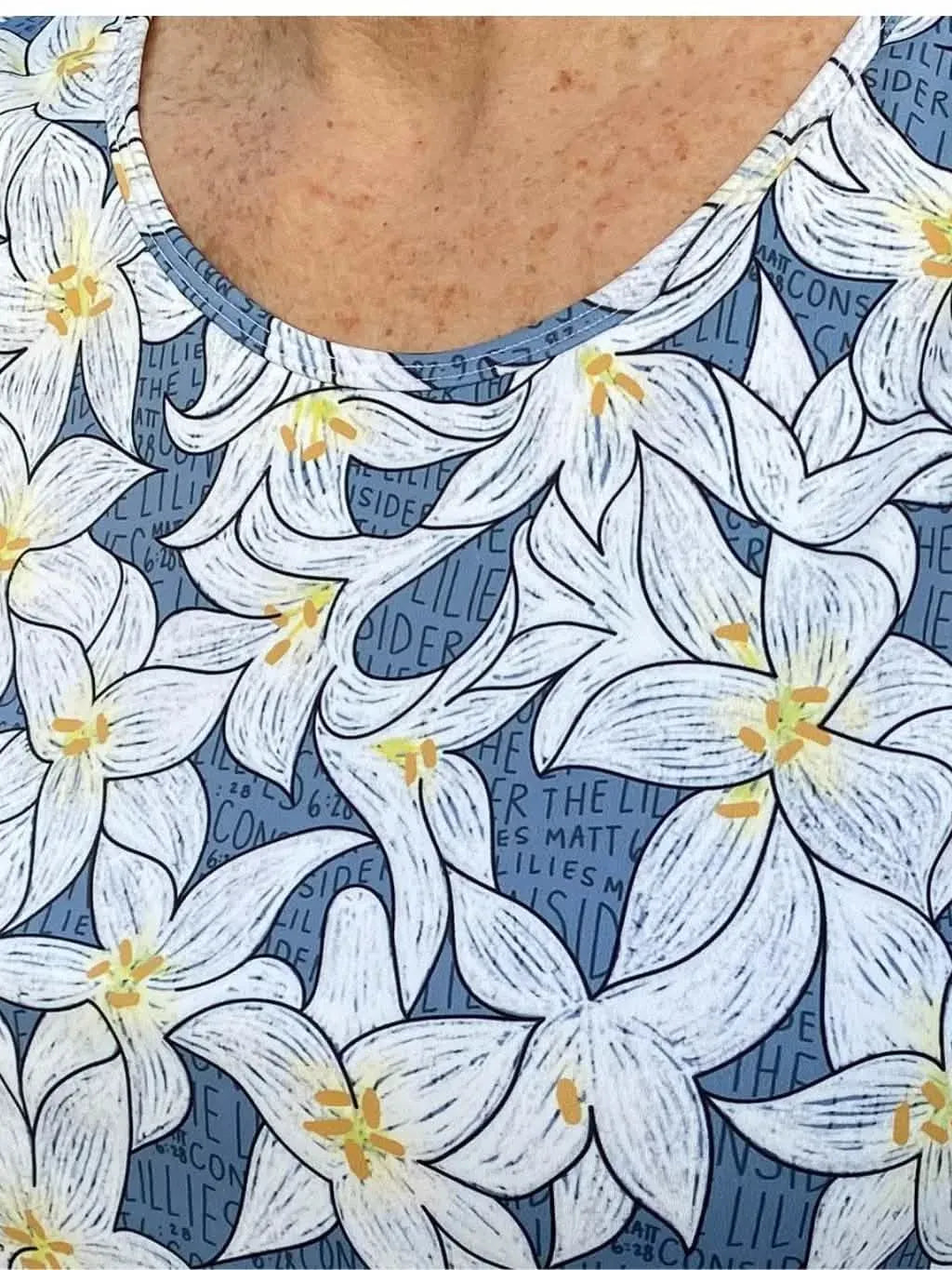 A person wears a blue tank top with a white lily floral pattern.
