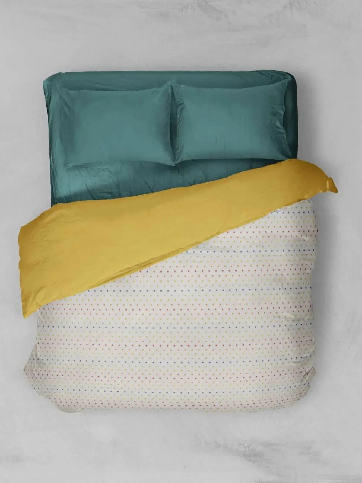 A bed with teal pillows and a yellow and rainbow star patterned duvet.
