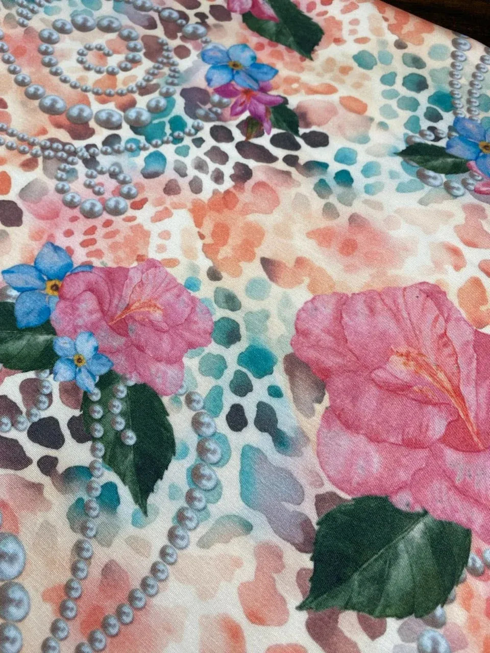 Fabric with pink hibiscus, blue flowers, pearls, and an abstract background.