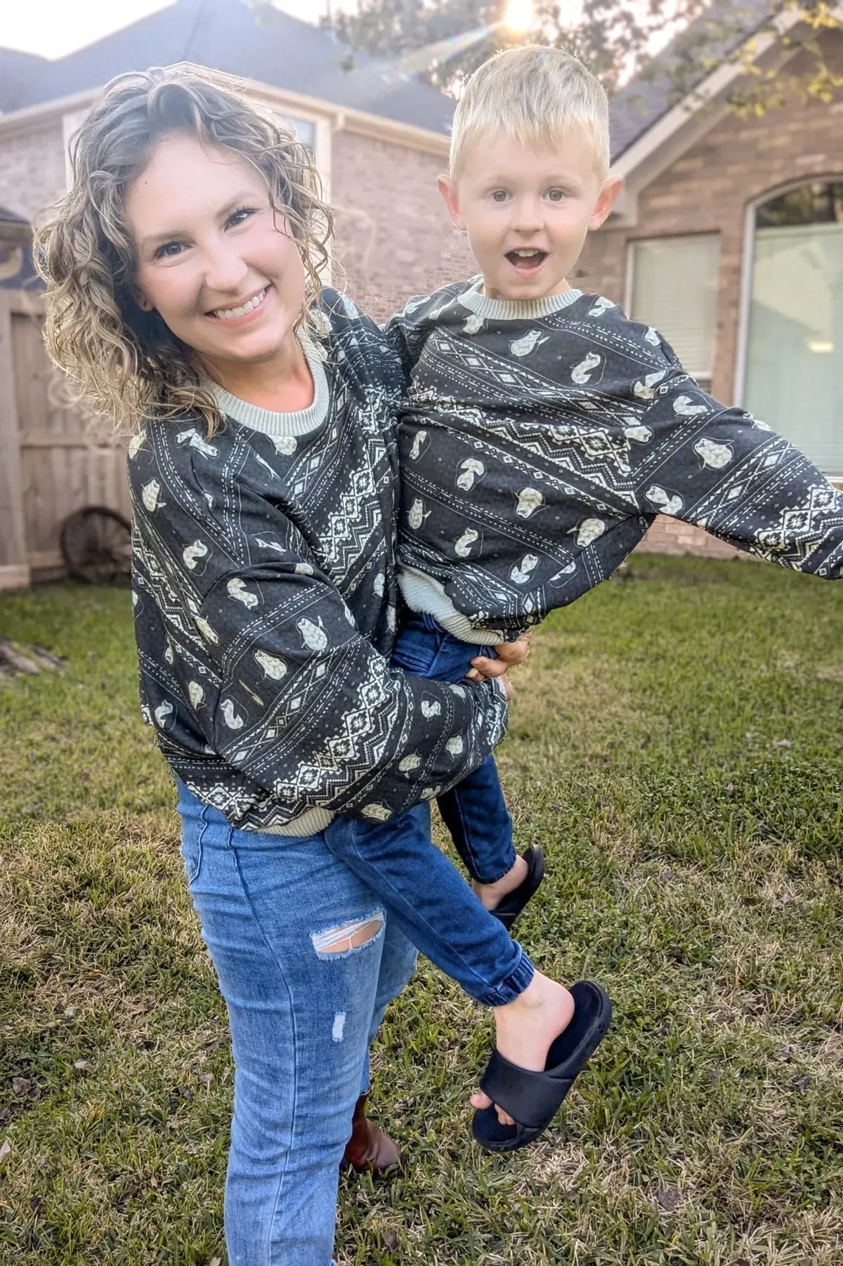 A woman holds a child, both wearing matching dark sweaters with a winter waddle pattern.