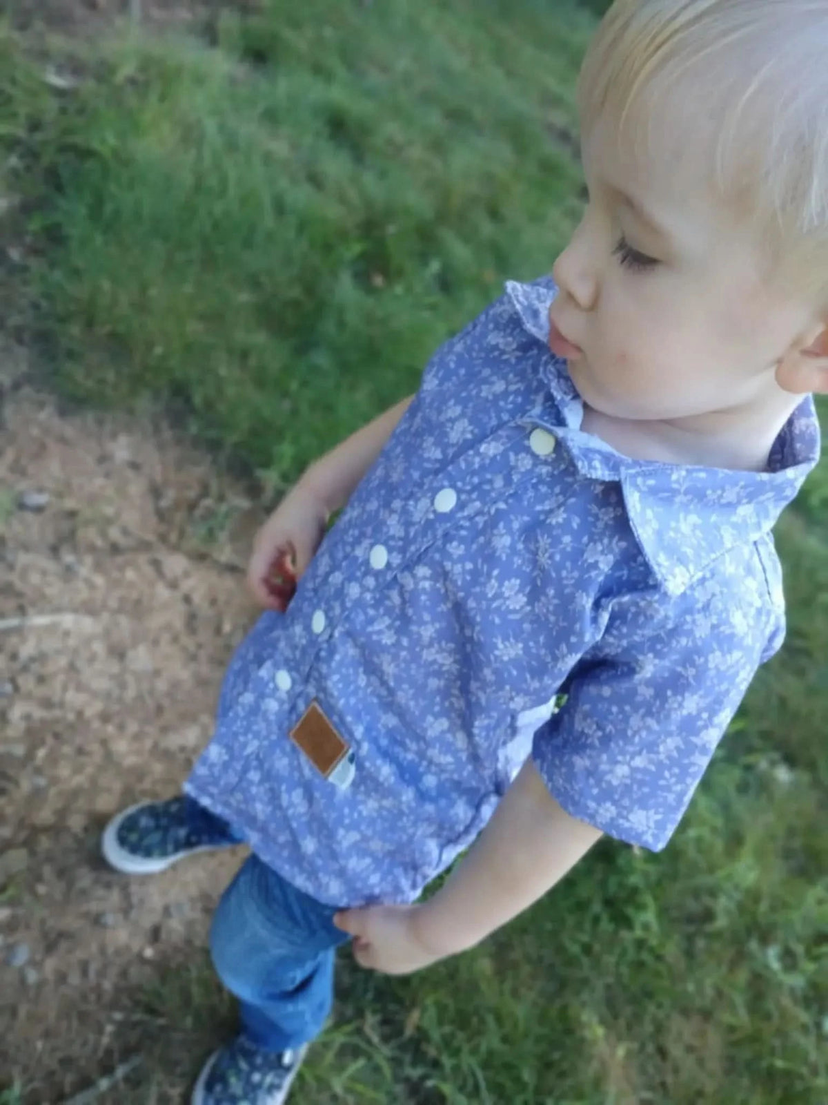 A child wears a blue floral shirt with white buttons and jeans.