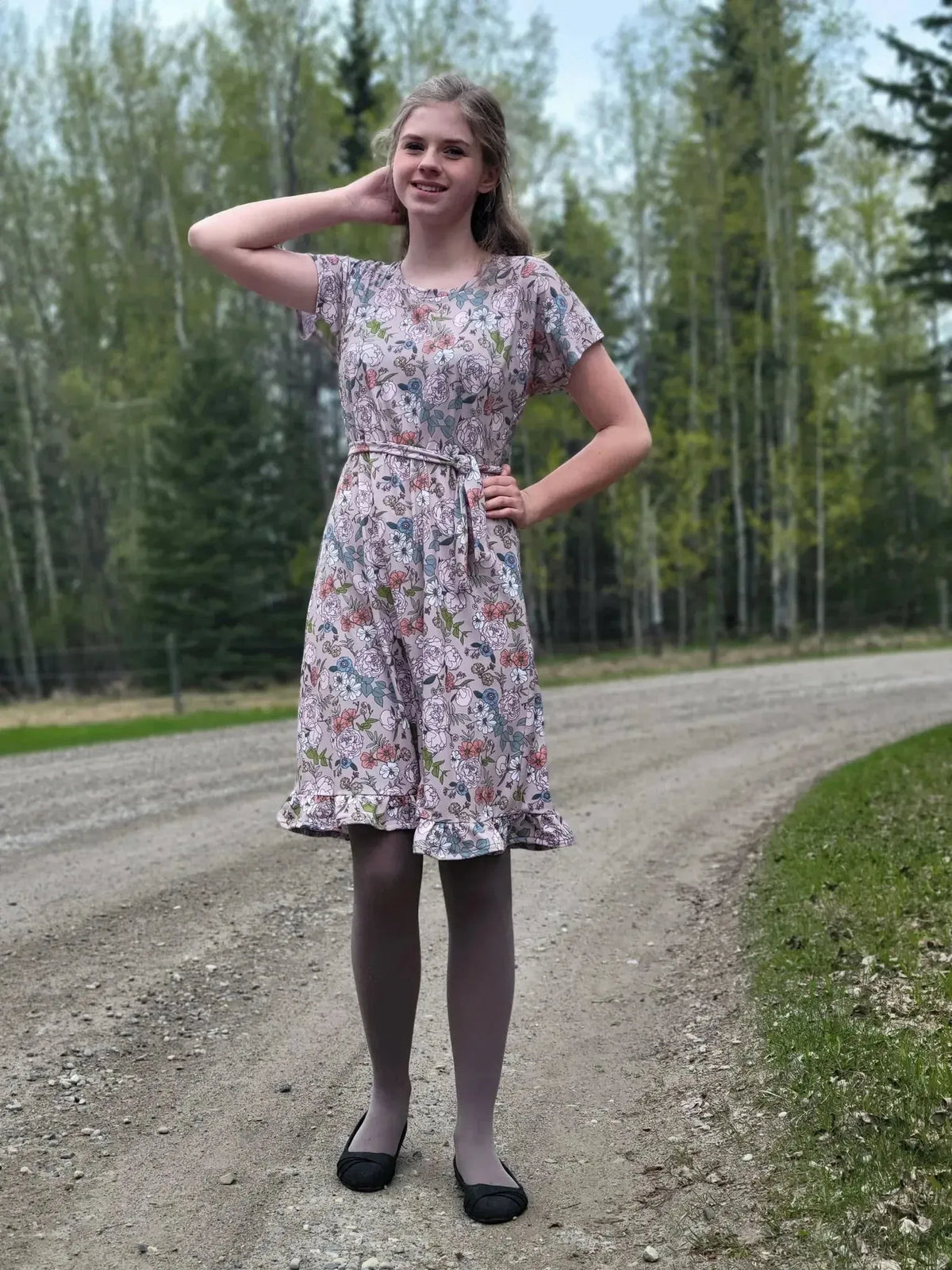 A young woman models a tan Japanese floral print dress in a forested setting.
