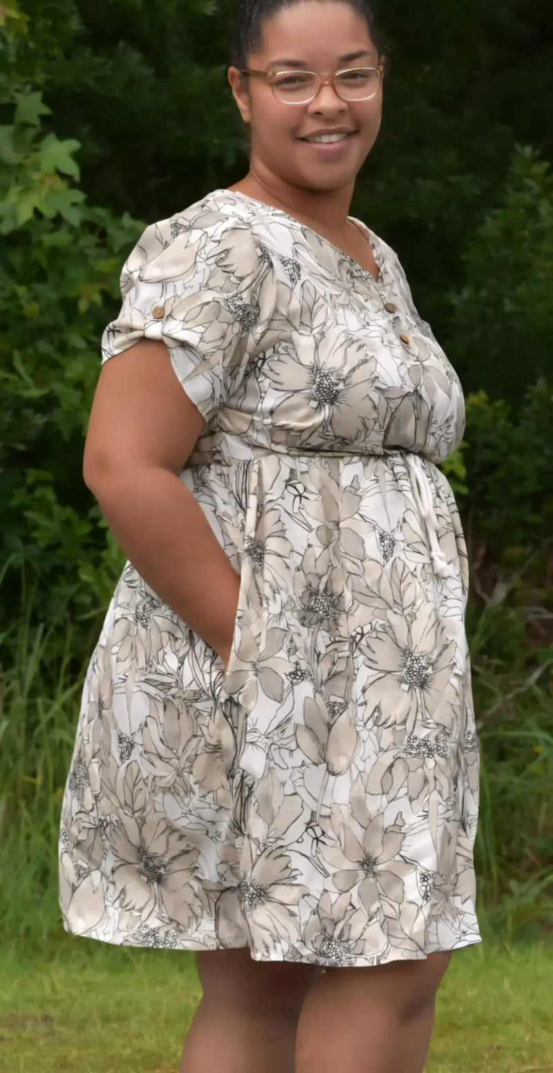 A woman in a sepia sketch floral dress with pockets smiles at the camera.