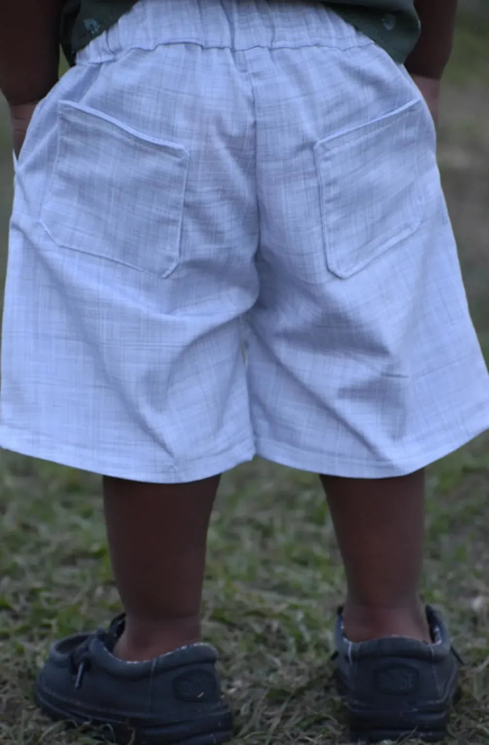 A child from behind wears light blue plaid shorts with two back pockets.