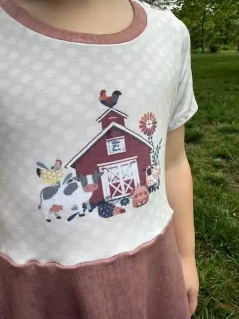 A child wears a shirt with a "Bless this Barn" panel featuring farm animals.