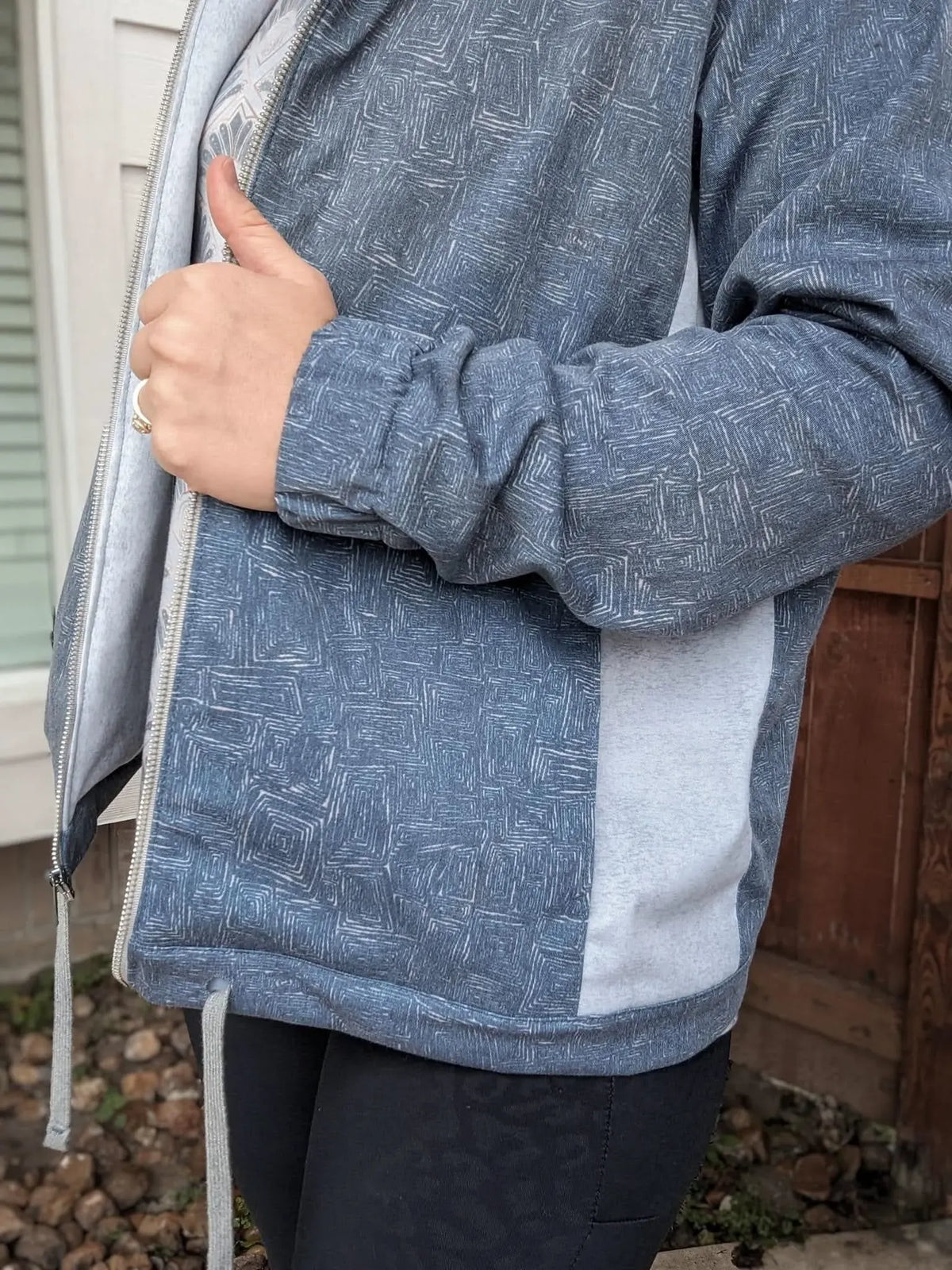 A person wears a blue and white patterned jacket with a thumb up.