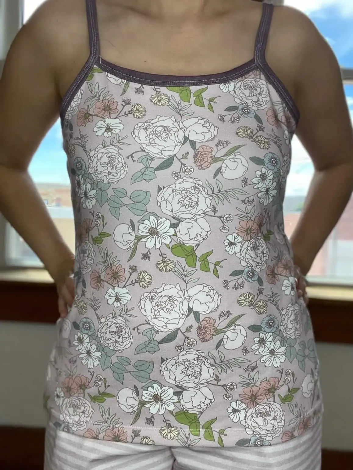 A person wears a mauve floral tank top with white, pink, and green flowers.