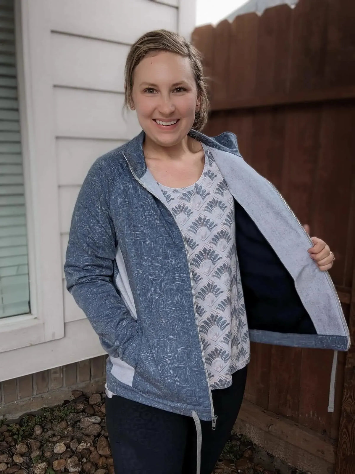 A woman smiles, wearing a blue patterned jacket over a light patterned top.