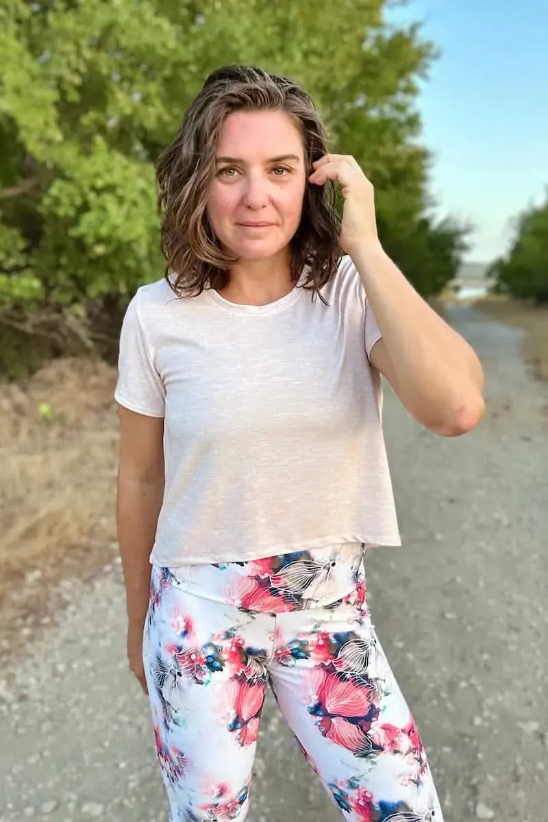 A woman wears a cream heather crop top and floral leggings.