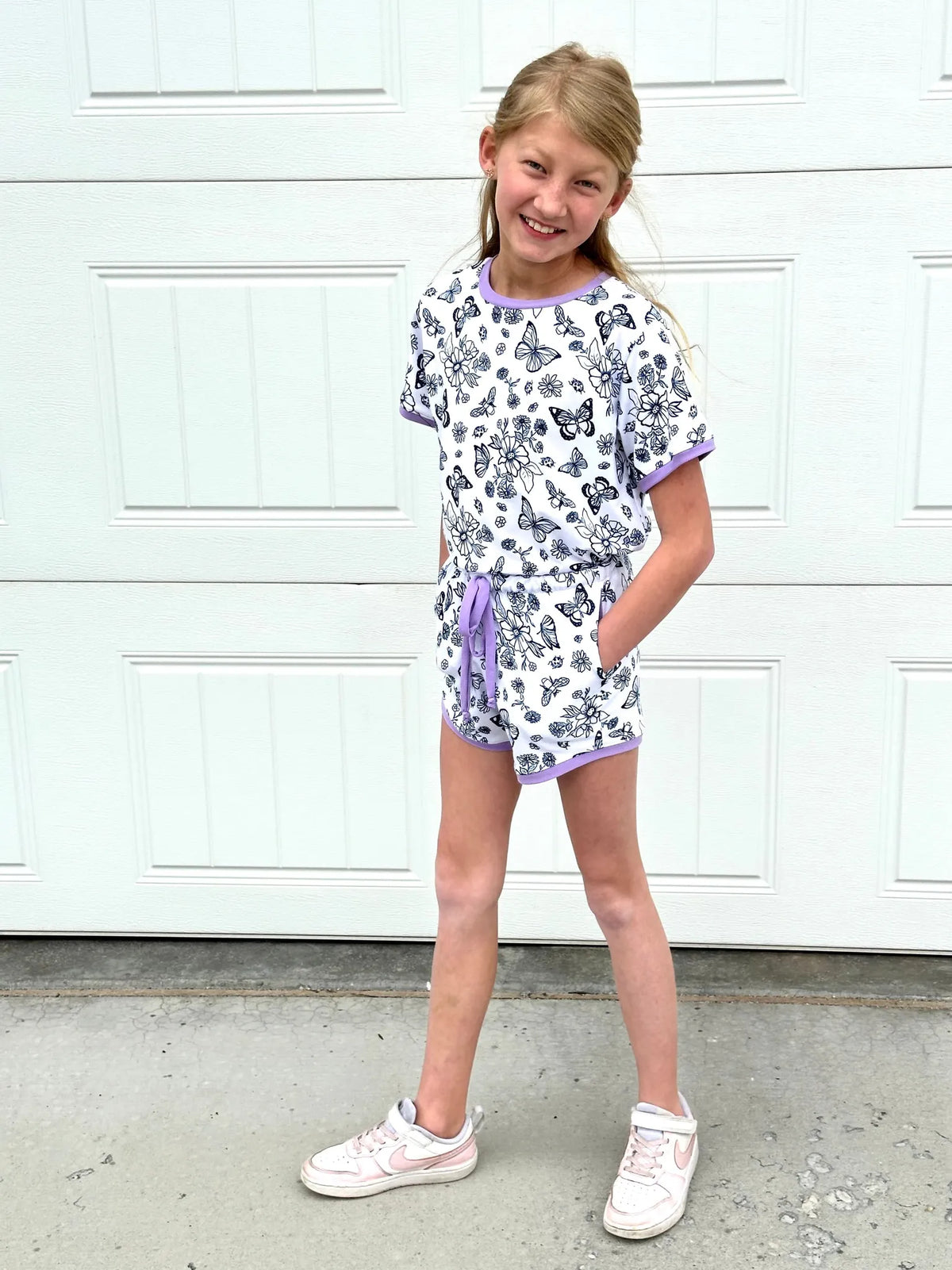 A young girl smiles, wearing a white butterfly and floral print top and shorts set.