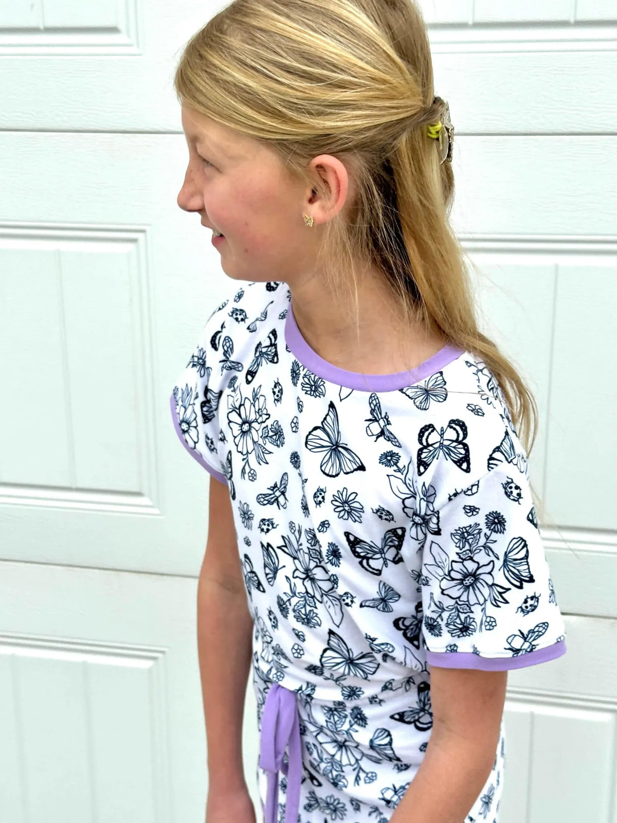 A young girl wears a white shirt with black butterfly and floral outlines.