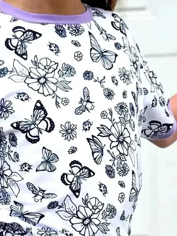 White fabric print with black line drawings of butterflies, daisies, and berries, plus purple trim.