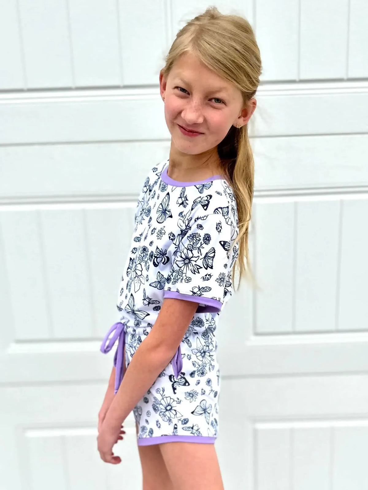 A young girl wears a white romper with a black and white butterfly pattern.