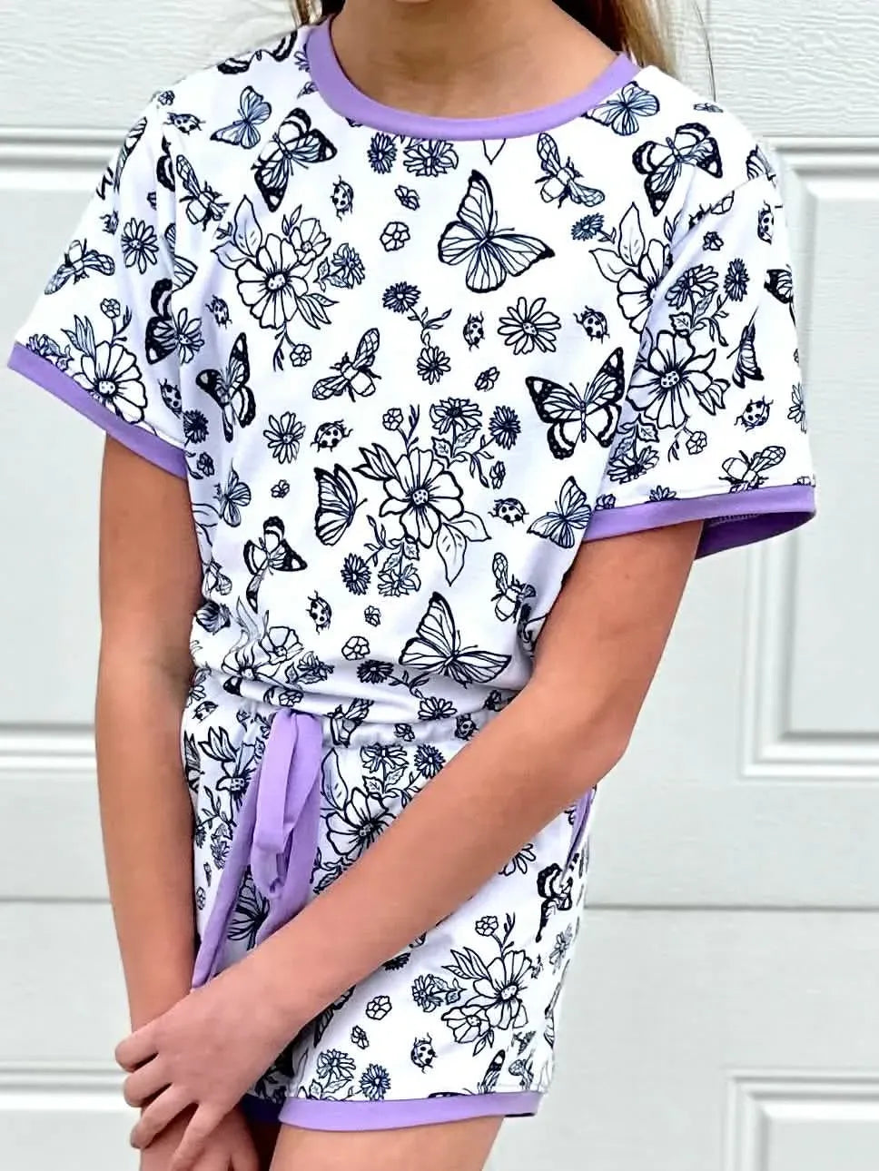A child wears a white outfit with black and blue butterfly and floral outlines.