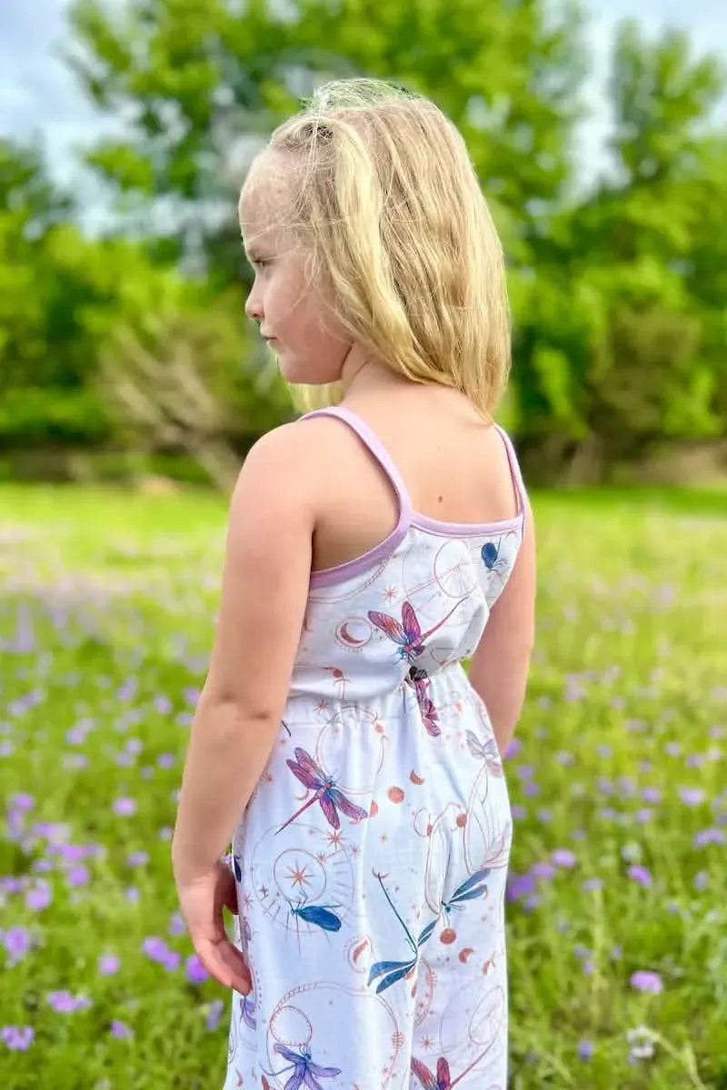 A young girl wears a white jumpsuit with a celestial dragonfly pattern.