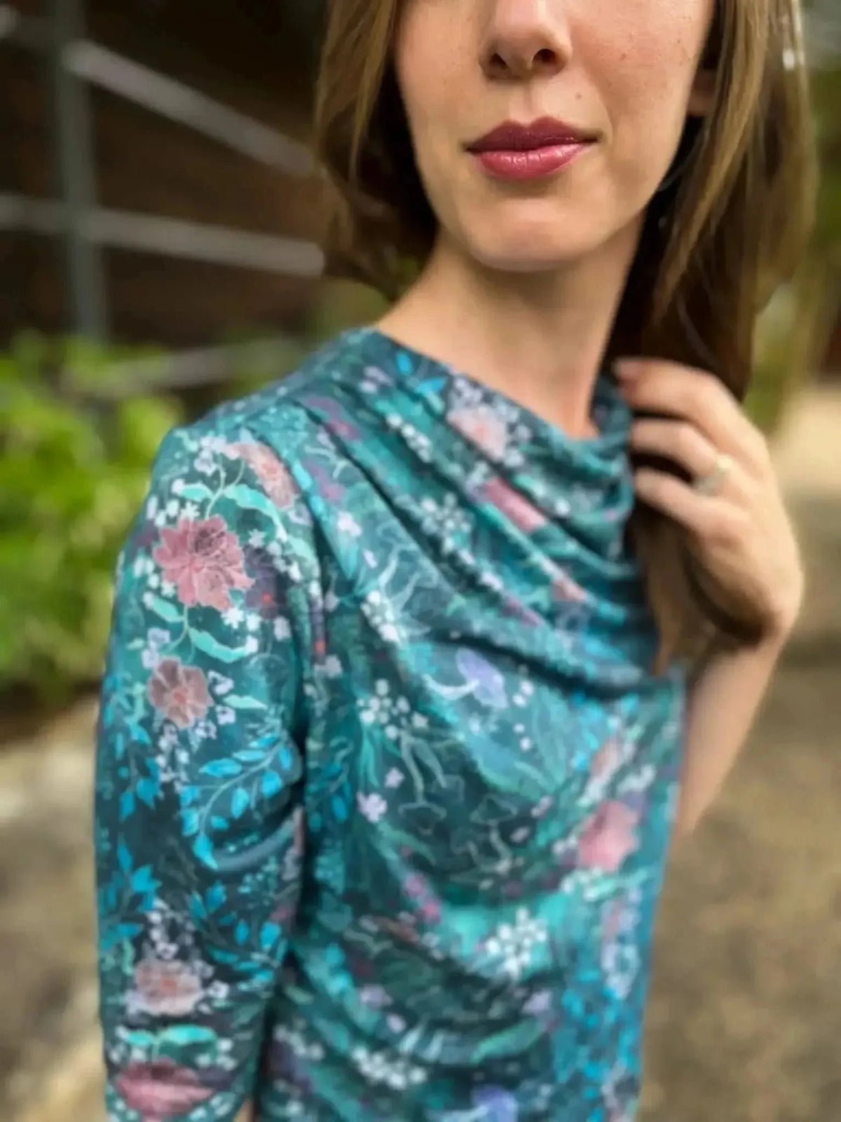 A woman wears a teal woodland print top with pink and white flowers.
