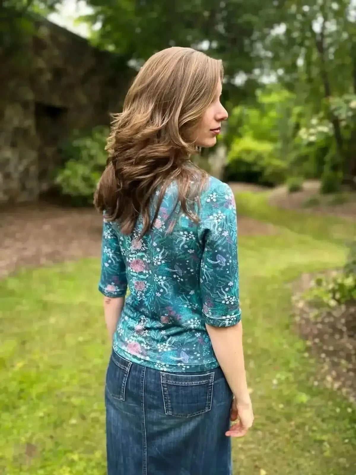 Teal woodland print fabric with enchanted glen pattern on a green outdoor background.