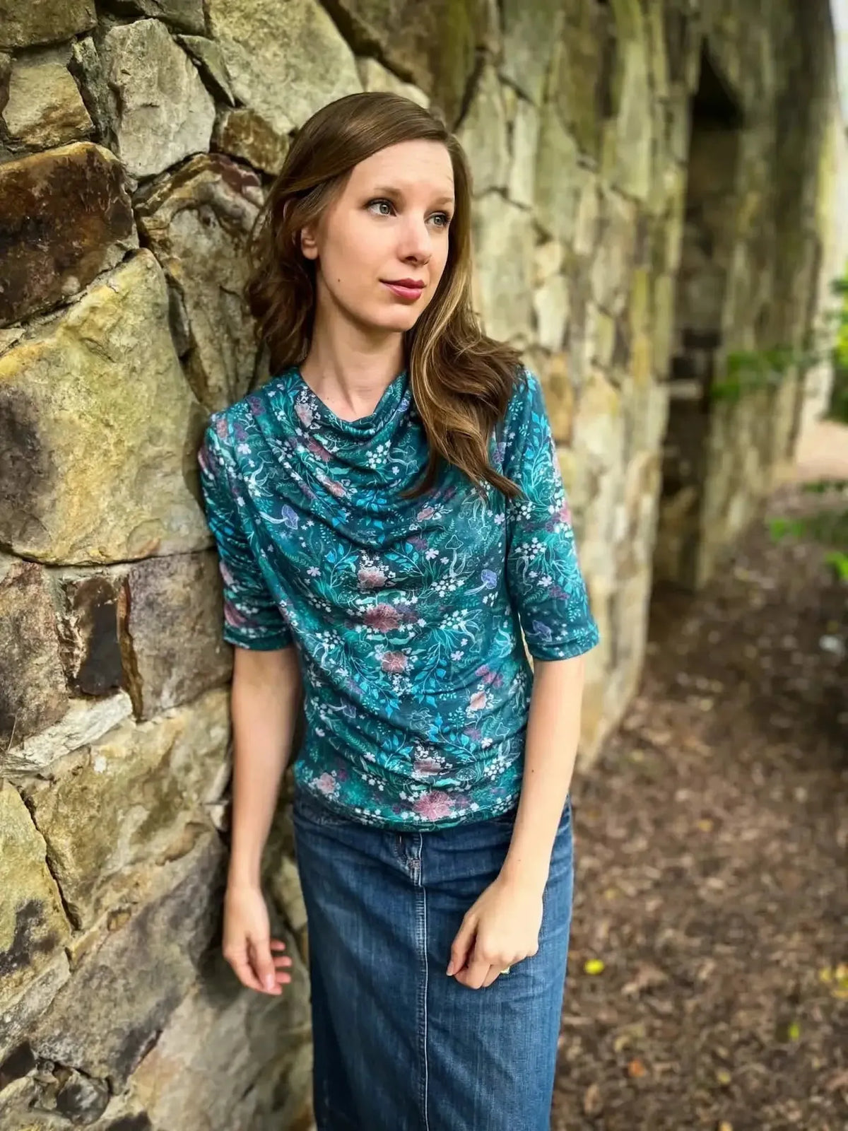 A woman wears a teal woodland print top and a denim skirt.