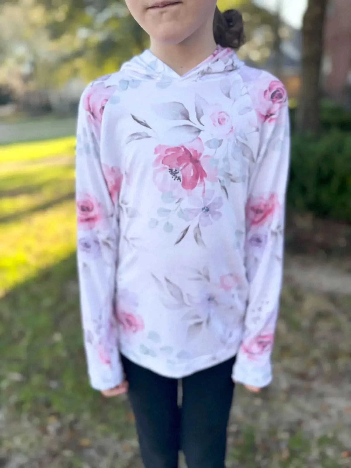 A child wears a white hoodie with a pink watercolor floral pattern and black pants.