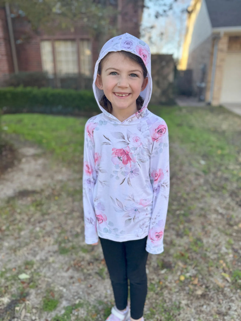 A young girl smiles wearing a white hoodie with a pink watercolor floral print.