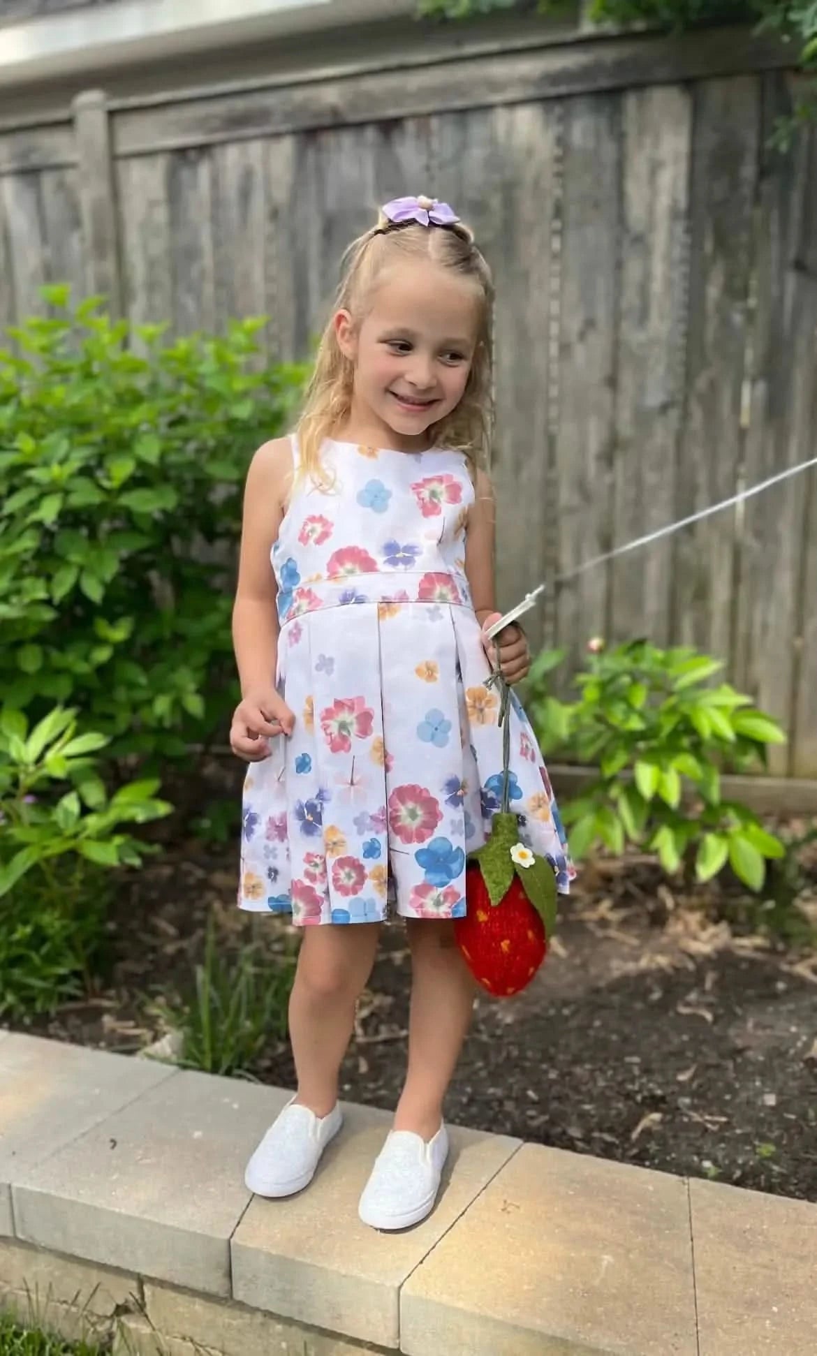 A young girl wears a white dress with a colorful pressed flower pattern.