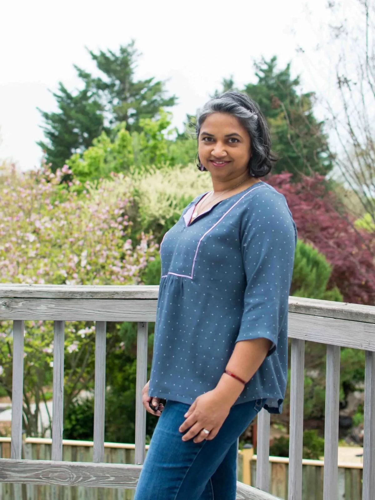 A woman in a navy polka dot top and jeans stands on a wooden deck.