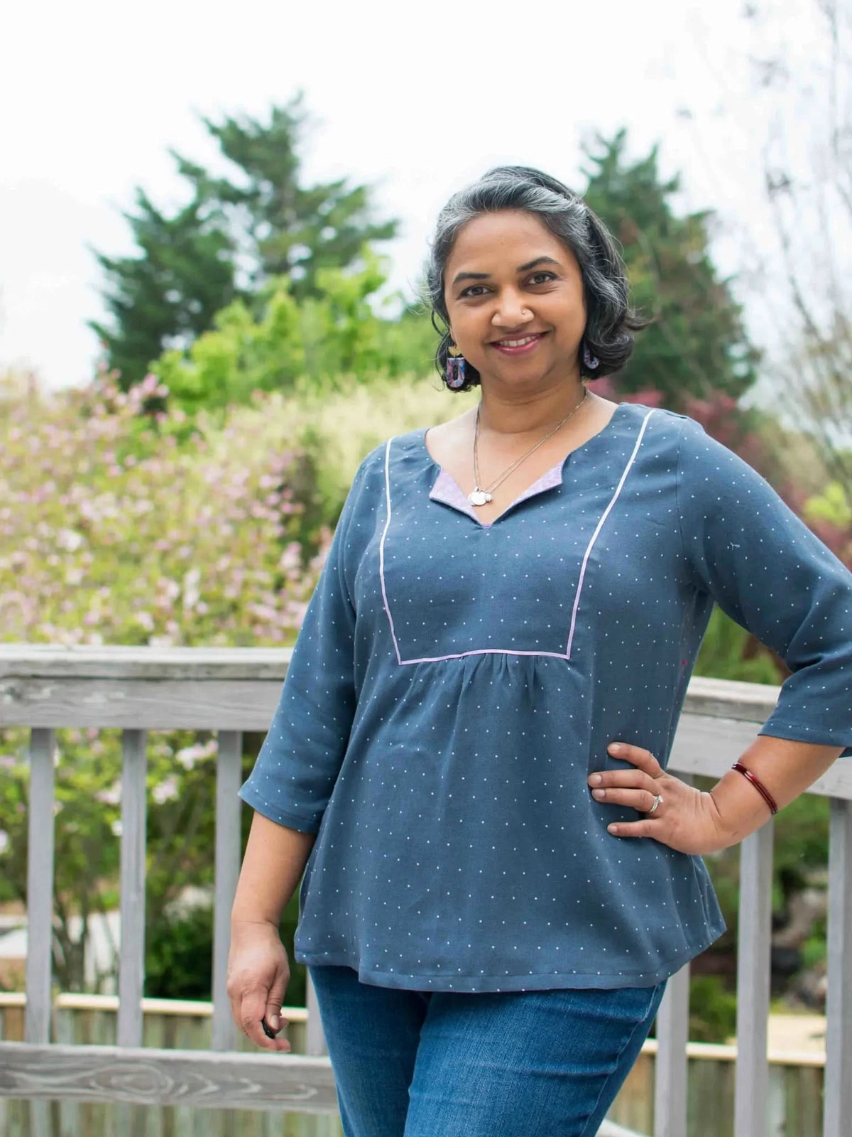 Woman wearing a navy polka dot top with pink trim and jeans.