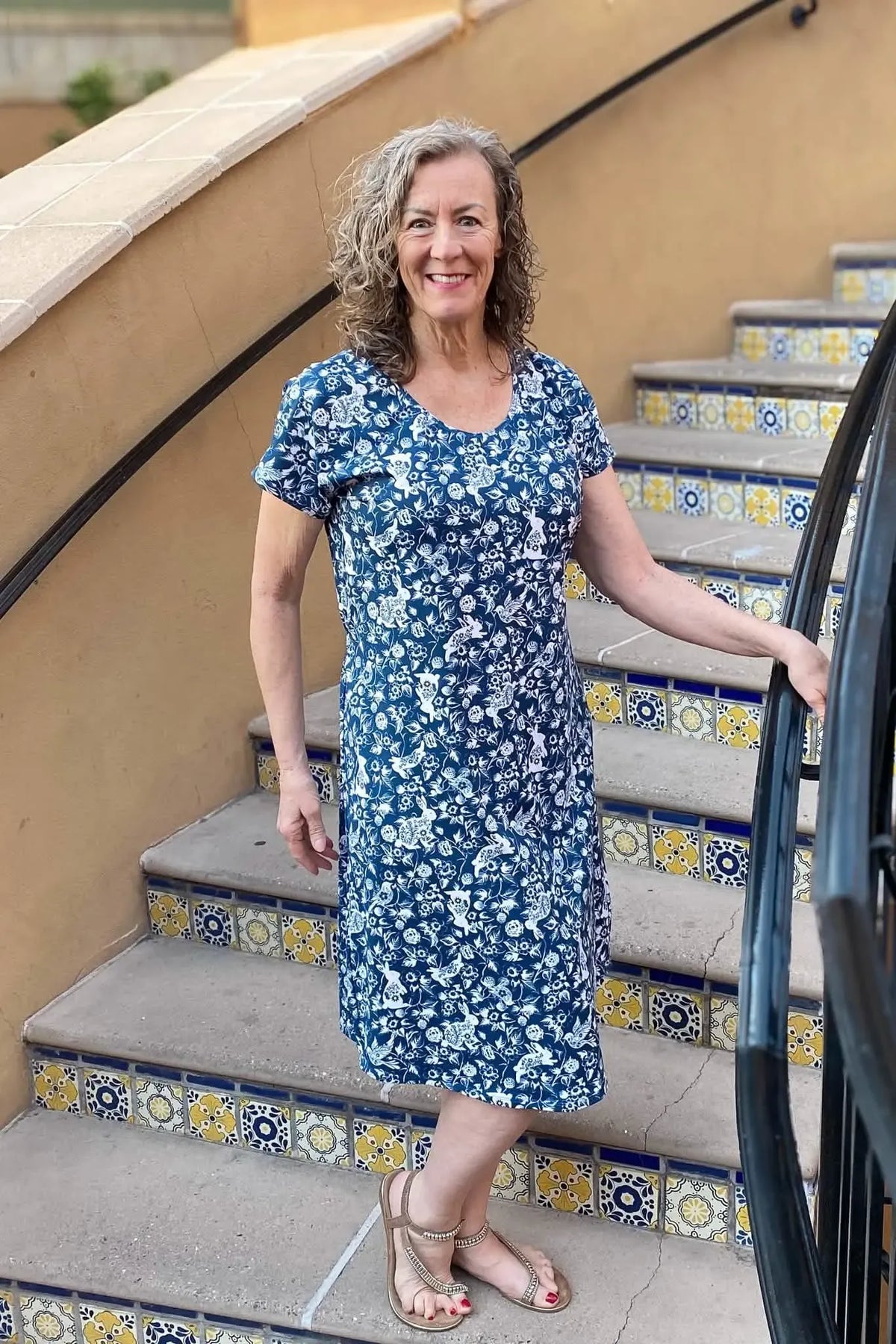A woman in a blue and white floral dress with bunny patterns stands on tiled stairs.