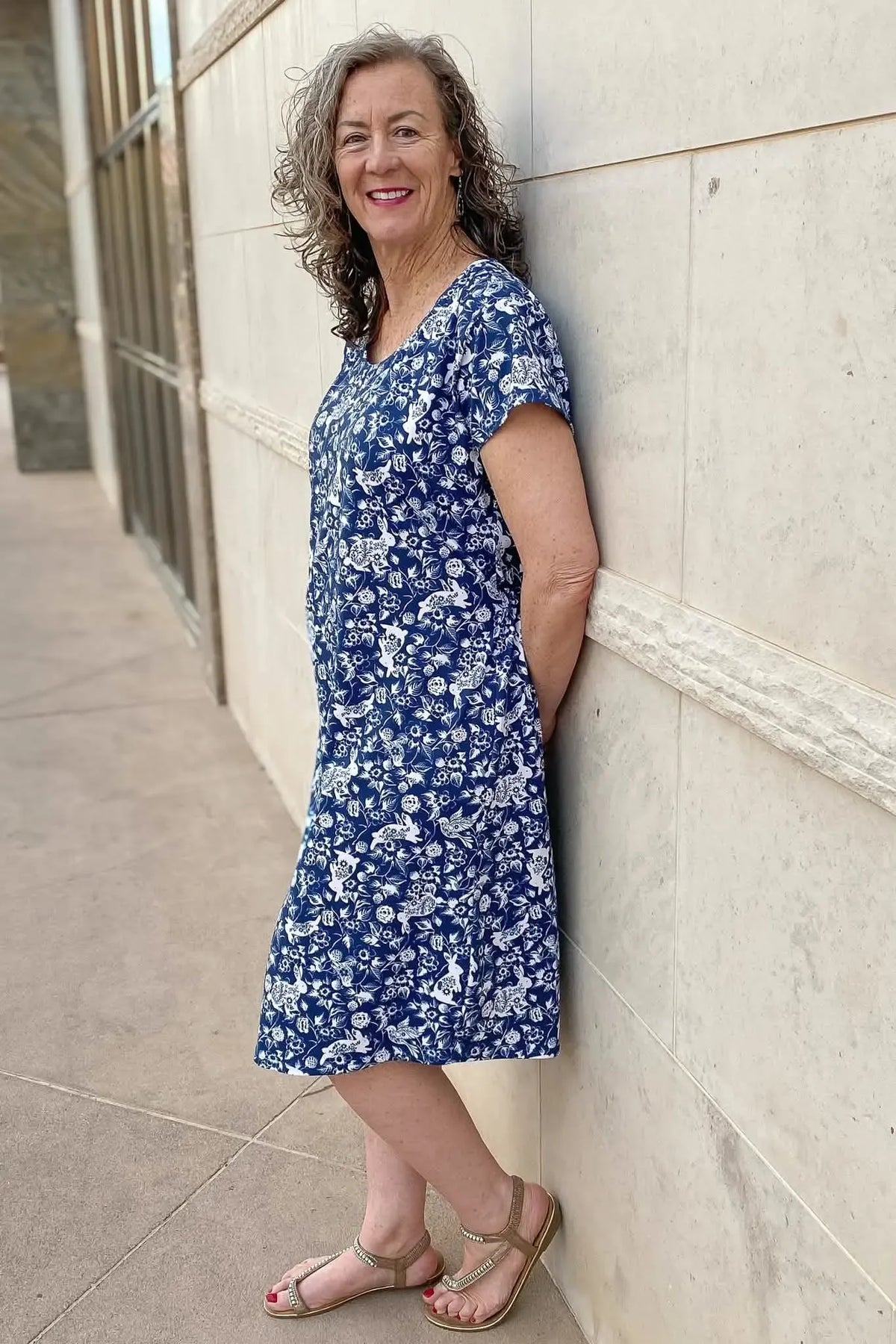 A woman in a blue and white floral dress with bunnies leans against a wall.