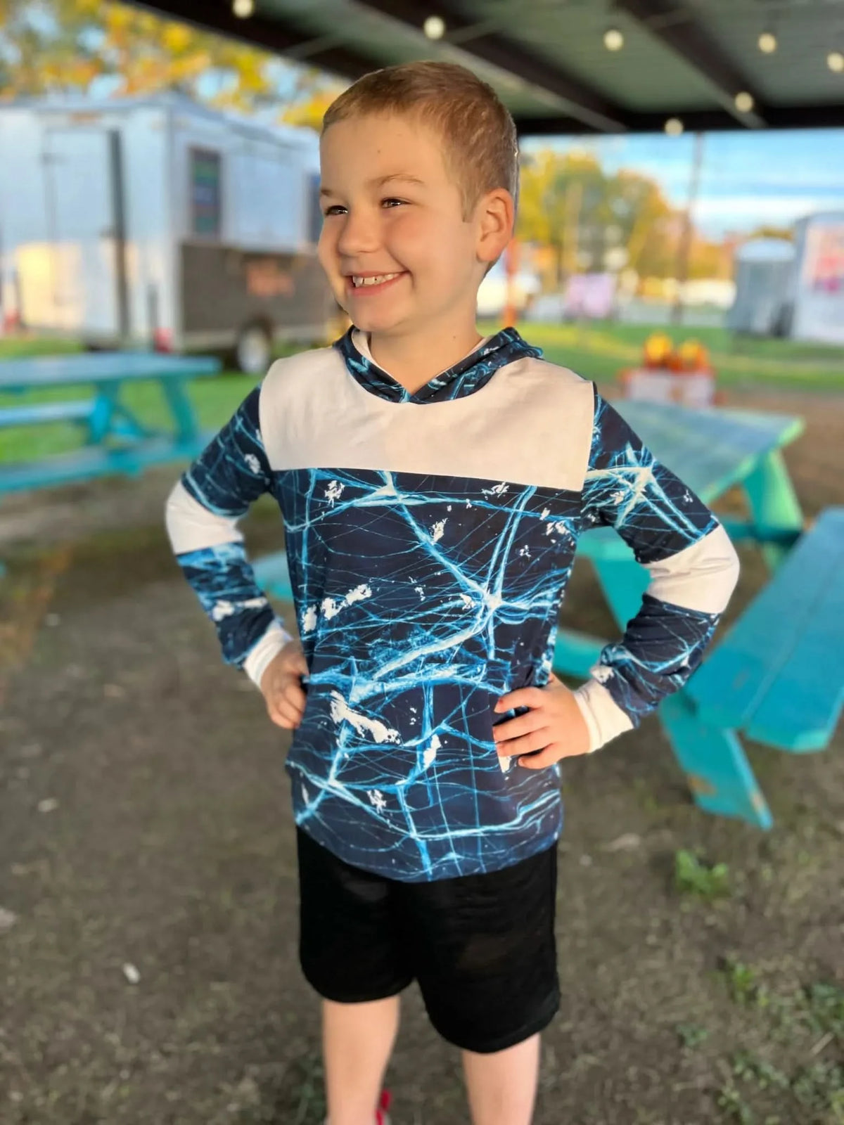 A boy wears a navy blue and white cracked ice patterned hoodie and black shorts.